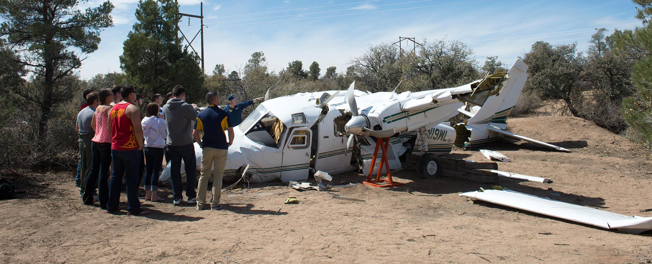 A group of students gather near a crashed plane