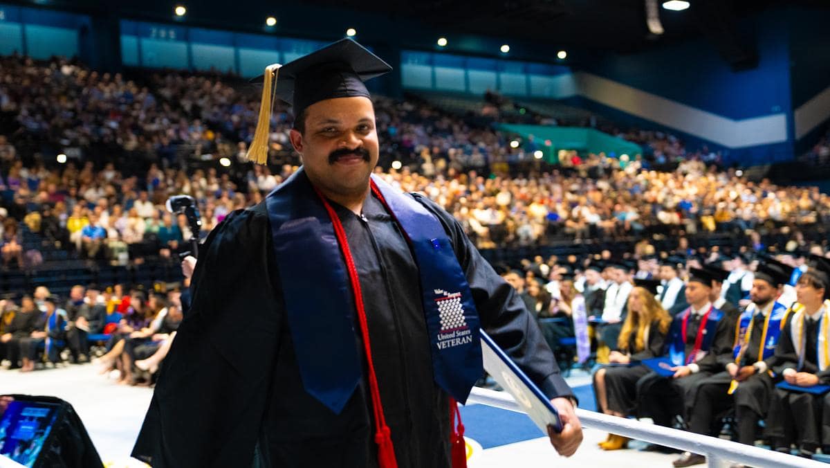 Student veteran in gown and cap in auditorium