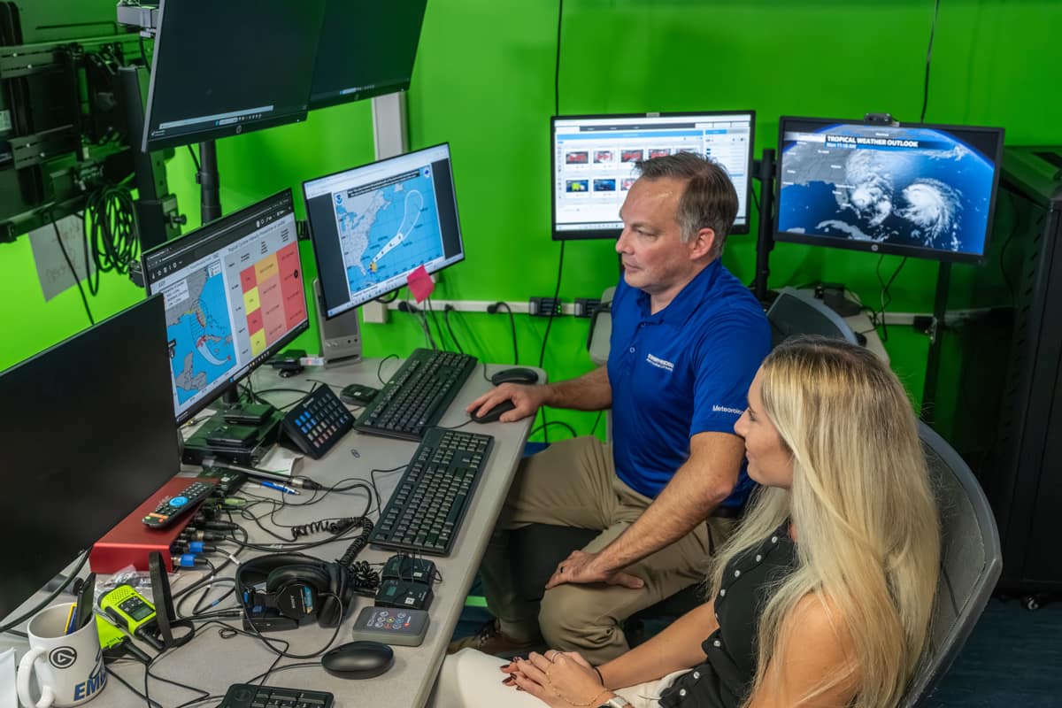 Dr. Rob Eicher and alumna Madison Croker review hurricane forecast graphics in Embry-Riddle’s Weather Broadcast Studio. The graphic to the left shows a new presentation of the cone of uncertainty with a brief chart listing various landfall locations and intensification potential at each.
