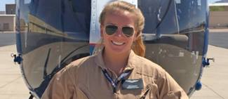 Pilot Leah Murphy stands in front of a helicopter, smiling