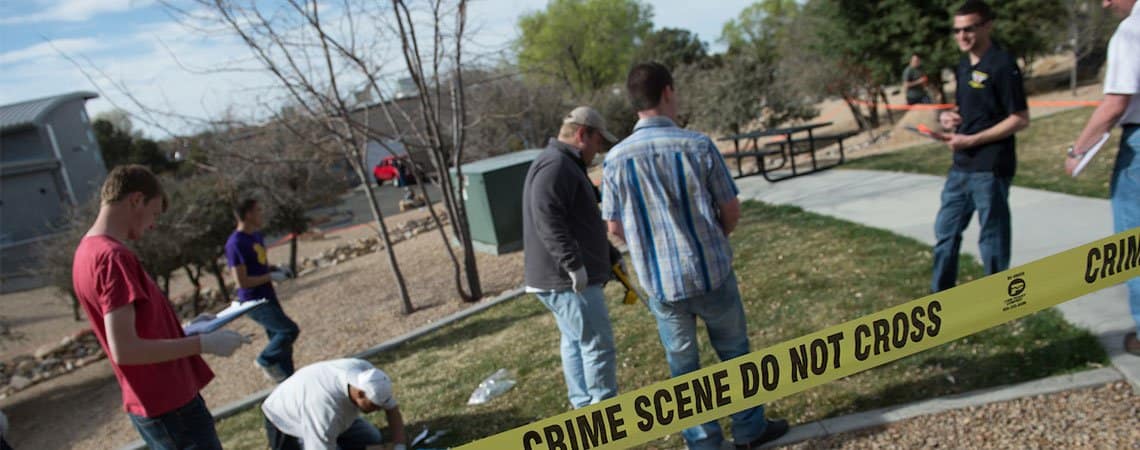 Students review a "crime scene" behind "Crime Scene Do Not Cross" tape.