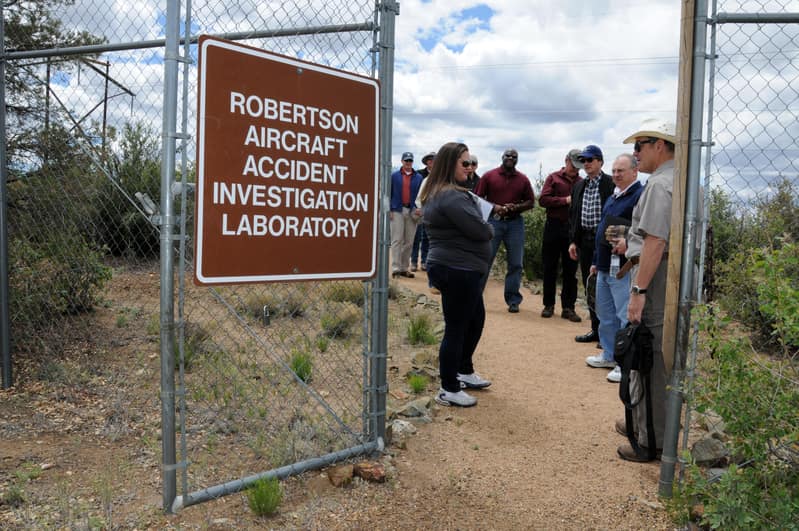 Students stand inside a fence with a sign that reads Robertson Aircraft Accident Investigation Laboratory.
