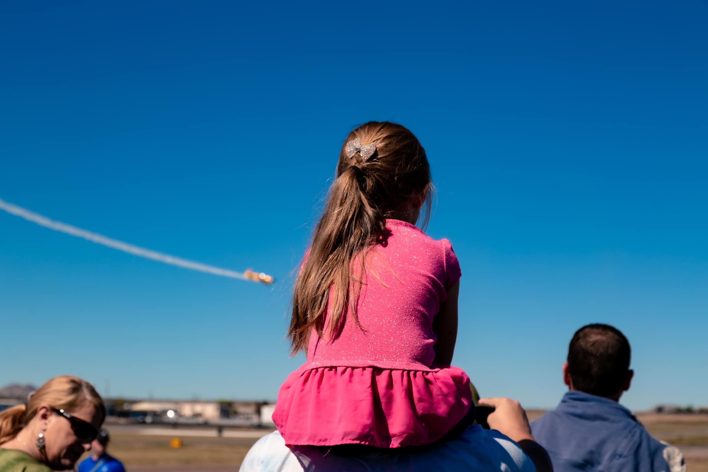 a child sits on an adult's shoulders to watch an air show
