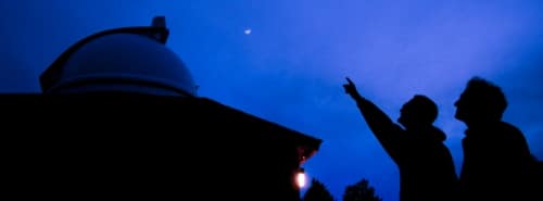 An Astronomy instructor points out particular stars and orbital bodies of interest to a student looking up at the night sky outside of campus' observatory